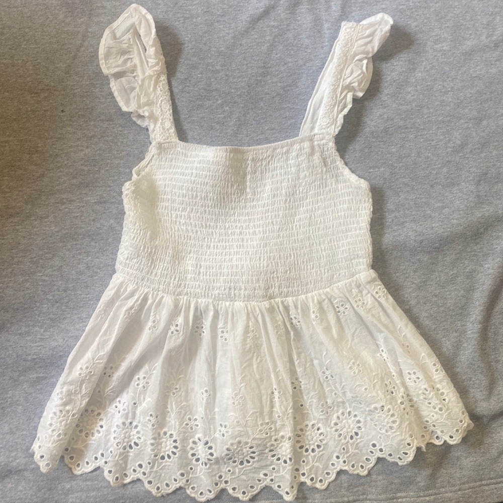 White tank top. Float, eyelet designs at bottom, ruffles by the straps.